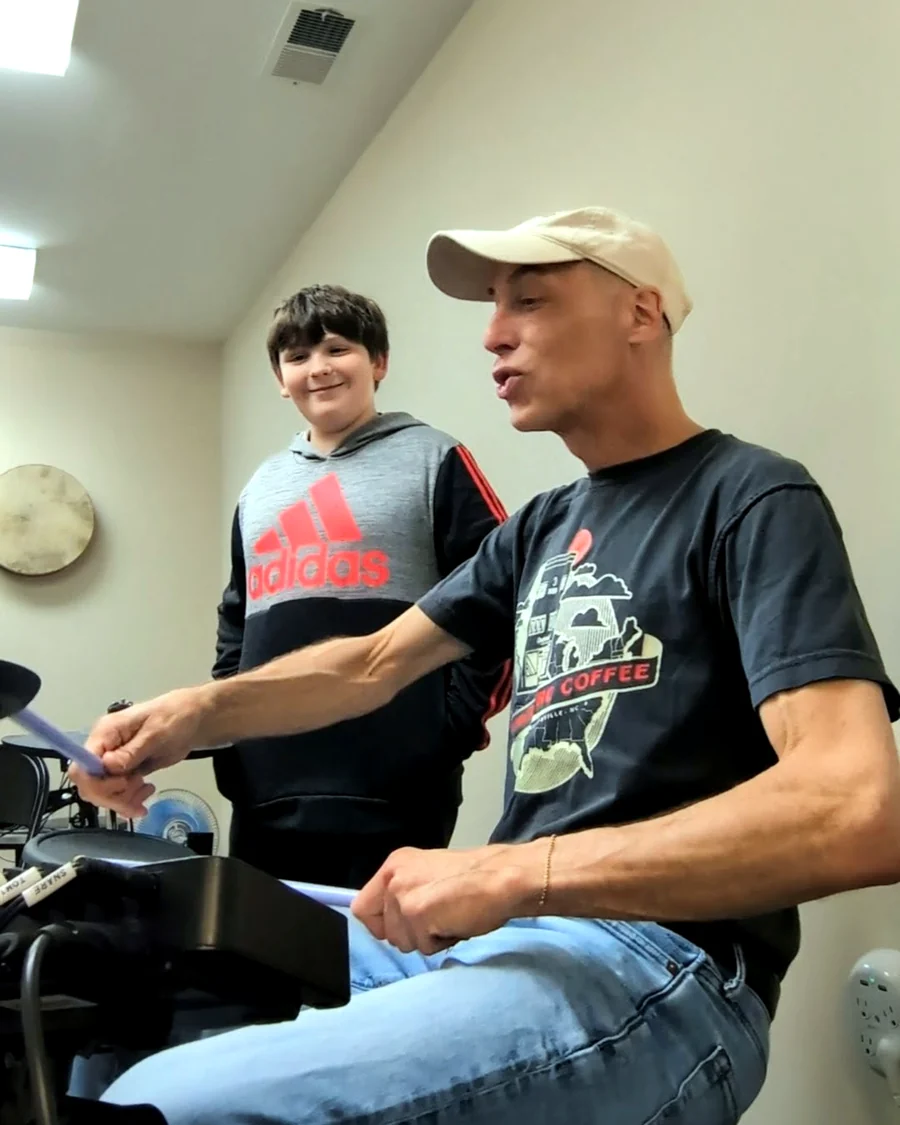 Teacher playing drums with a student beside him in the studio